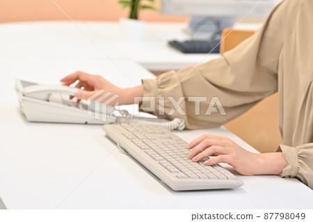 一個女人在敲鍵盤時伸手去拿聽筒 一個女人在敲鍵盤時伸手去拿聽筒 87798049