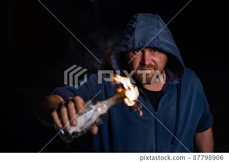 The man in the hood is holding a burning bottle. Molotov cocktail. 87798906