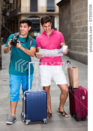 positive men are walking with photocamera and searching way to historical sight in map in Barcelona 87800506