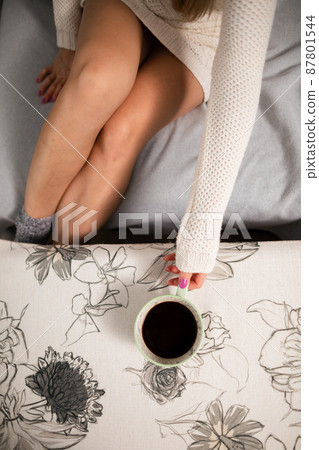 The slim legs of a shapely girl. She is holding a cup of hot coffee. The slim legs of a shapely girl. She is holding a cup of hot coffee. 87801544