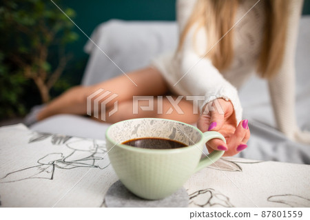 The slim legs of a sexy girl. She is holding a cup of hot coffee. 87801559