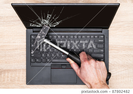 Hand breaking laptop screen with a hammer Hand breaking laptop screen with a hammer 87802482