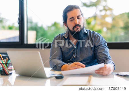 Young entrepreneur consulting documents while working at home Young entrepreneur consulting documents while working at home 87803449