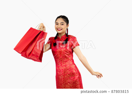 Chinese new year in shopping concept, Asian girl in red cheongsam costume smiling and holding shopping bags isolated on white background. 87803815