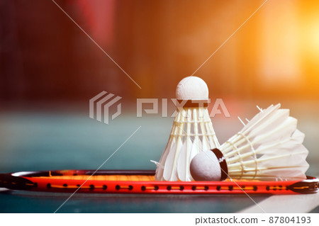 Cream white badminton shuttlecock and racket with neon light shading on green floor in indoor badminton court, blurred badminton background, copy space. 87804193