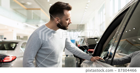 male buyer chooses a new car in a car dealership inspects the car 87804466