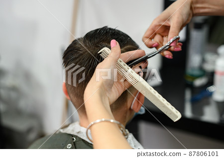 A teenager in a beauty salon gets a haircut, a hairdresser cuts a teenage boy's hair. 87806101