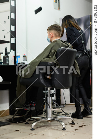 A teenager in a beauty salon gets a haircut, a hairdresser cuts a teenage boy's hair. 87806102
