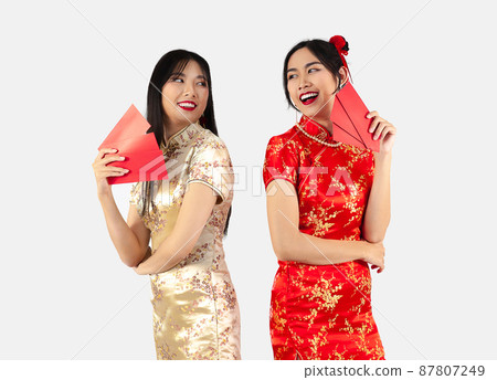 Chinese new year concept Two Asian women in red traditional oriental costume holding red envelopes or Ang Pow isolated on white background.. Chinese new year concept Two Asian women in red traditional oriental costume holding red envelopes or Ang Pow isolated on white background.. 87807249