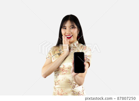 Asian woman in gold traditional oriental costume holding smartphone with black screen on white background. Chinese new year concept. Asian woman in gold traditional oriental costume holding smartphone with black screen on white background. Chinese new year concept. 87807250