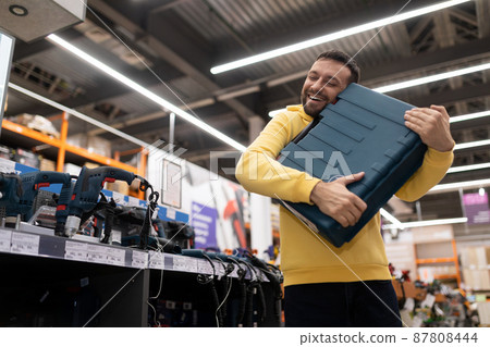 happy buyer of a new electric drill hugging the box in awe in a hardware store happy buyer of a new electric drill hugging the box in awe in a hardware store 87808444