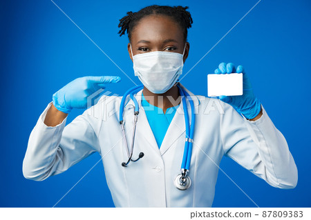 African american doctor woman hold blank empty business card in blue studio African american doctor woman hold blank empty business card in blue studio 87809383