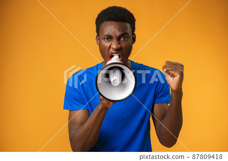 Young black man shouting in megaphone on yellow background 87809418