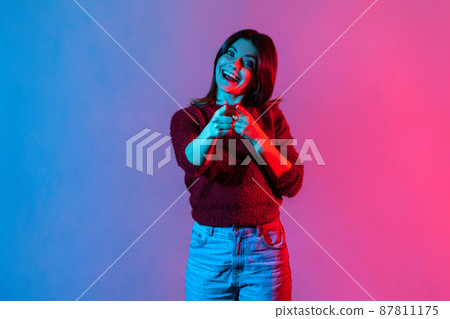 Hey, you are awesome. Neon light portrait of happy optimistic woman pointing direction to camera and smiling broadly, noticing you lucky winner, making choice with finger. indoor studio shot isolated 87811175