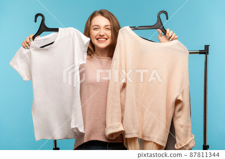 Lovely cheerful woman shopper holding clothes on racks and looking with toothy smile, enjoying shopping in modern boutique, choosing trendy outfit, updating wardrobe. indoor studio shot isolated Lovely cheerful woman shopper holding clothes on racks and looking with toothy smile, enjoying shopping in modern boutique, choosing trendy outfit, updating wardrobe. indoor studio shot isolated 87811344