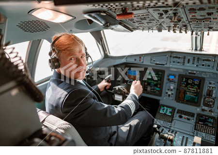Male pilot in headphones sitting in airplane cockpit 87811881