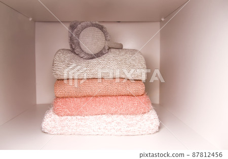 White shelf of the home wardrobe with colorful sweaters, jumpers and warm headphones. Small space organization White shelf of the home wardrobe with colorful sweaters, jumpers and warm headphones. Small space organization 87812456