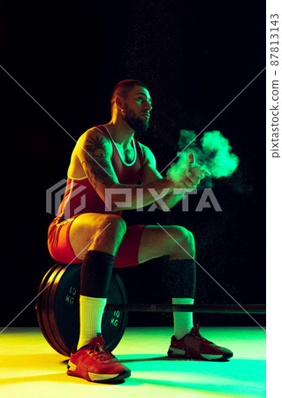 One young man, professional weightlifter sportswear training with barbell isolated dark background in neon. Sport, weightlifting, power, achievements concept 87813143