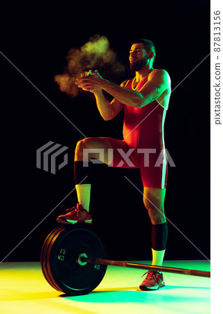 One young man, professional weightlifter sportswear training with barbell isolated dark background in neon. Sport, weightlifting, power, achievements concept One young man, professional weightlifter sportswear training with barbell isolated dark background in neon. Sport, weightlifting, power, achievements concept 87813156