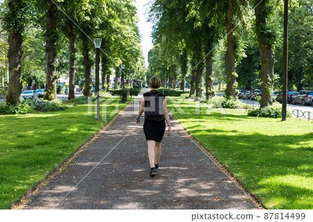 Attractive woman in black dress walking in a green city park 87814499