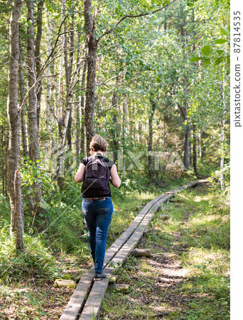 Young healthy woman with backpack walking over a wooden path in the Florarna Naturreservat Young healthy woman with backpack walking over a wooden path in the Florarna Naturreservat 87814535