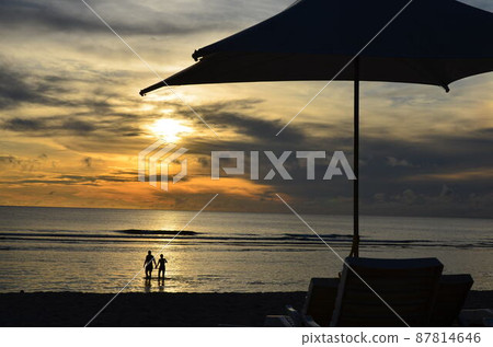Sunset seen from the beach, couple and beach umbrella 1 87814646