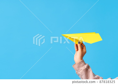 A woman's hand holds yellow paper airplane on blue background A woman's hand holds yellow paper airplane on blue background 87818325