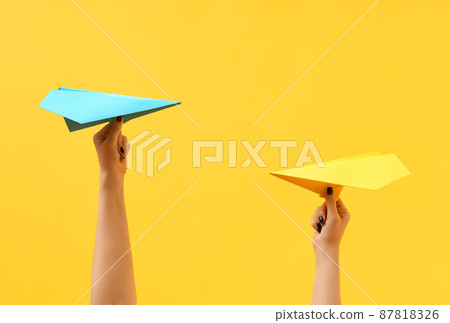 A woman's hands holds multicolored paper airplanes on yellow background A woman's hands holds multicolored paper airplanes on yellow background 87818326