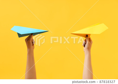 A woman's hands holds multicolored paper airplanes on yellow background A woman's hands holds multicolored paper airplanes on yellow background 87818327