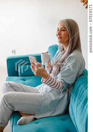 Woman using cellphone and drinking coffee at home 87819171