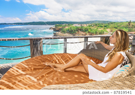 Young woman relaxing in lounge on veranda with sea view Young woman relaxing in lounge on veranda with sea view 87819541