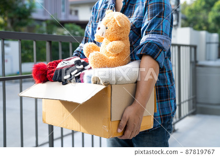 Holding clothing donation box with used clothes and doll at home to support help for poor people in the world. Holding clothing donation box with used clothes and doll at home to support help for poor people in the world. 87819767