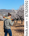 Young modern farmer with axe on his shoulder tree field in the background 87820092
