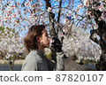 Long-haired young man smelling flowers from the tree in an almond grove 87820107