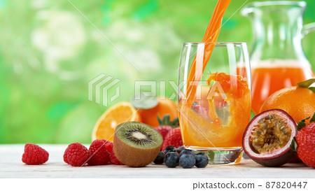 Multivitamin juice pouring into glass. Fresh orange juice with oranges fruit on wooden table. Multivitamin juice pouring into glass. Fresh orange juice with oranges fruit on wooden table. 87820447