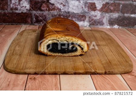 Homemade roll with poppy seeds on a wooden board on the table. 87821572