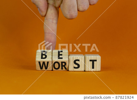 Best or worst symbol. Businessman turns wooden cubes and changes the word best to worst. Beautiful orange table, orange background, copy space. Business and best or worst concept. 87821924
