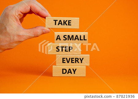 Take a small step every day symbol. Wooden blocks with words Take a small step every day. Businessman hand. Beautiful orange background, copy space. Business, step every day concept. 87821936