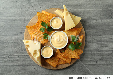 Board with cheese sauce, chips, cheese and parsley on gray textured table 87822036
