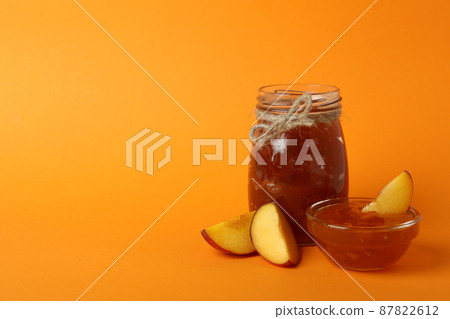 Jar and bowl of peach jam and ingredients on orange background 87822612