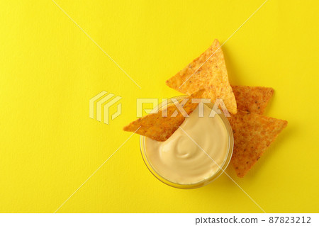 Bowl with cheese sauce and chips on yellow background Bowl with cheese sauce and chips on yellow background 87823212
