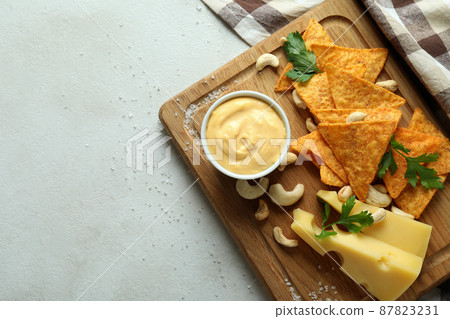 Board with cheese sauce and snacks on white textured table 87823231