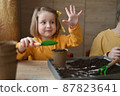 concept of gardening. little girl is engaged in planting seeds for seedlings, pouring earth into pots for growing crops. 87823641