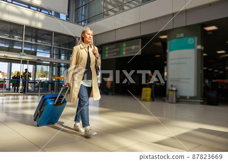 Female traveler carrying trolley luggage bag at airport 87823669