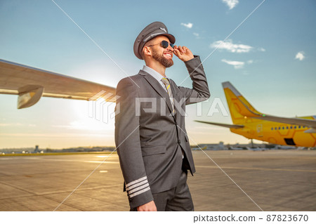 Joyful aircraft pilot standing outdoors at airfield Joyful aircraft pilot standing outdoors at airfield 87823670
