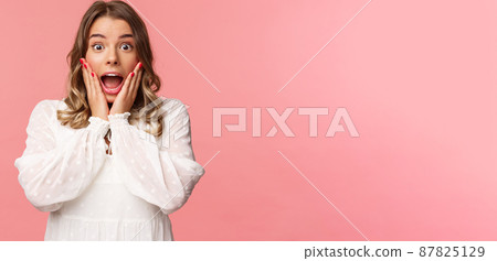 Happy and surprised blond girl hear awesome news, gasping speechless staring camera with hands on cheeks, being impressed and stunned over great event, standing pink background Happy and surprised blond girl hear awesome news, gasping speechless staring camera with hands on cheeks, being impressed and stunned over great event, standing pink background 87825129