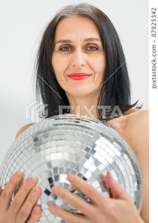 Studio photo of middle aged woman starting getting grey-haired wearing black clothes with silver disco ball in hands on white background, middle age sexy lady, happy life concept Studio photo of middle aged woman starting getting grey-haired wearing black clothes with silver disco ball in hands on white background, middle age sexy lady, happy life concept 87825342