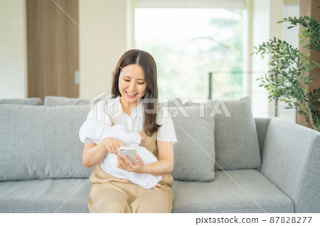 A woman who uses a smartphone while holding a baby A woman who uses a smartphone while holding a baby 87828277