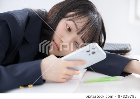 High school girl tired of studying and looking at her smartphone High school girl tired of studying and looking at her smartphone 87829785