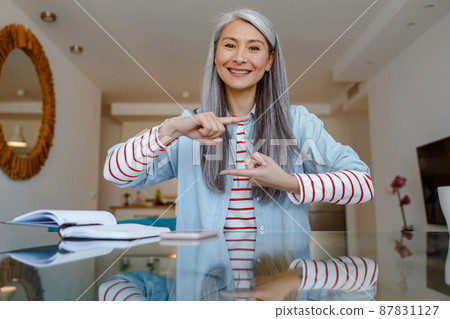 Woman sitting at the table and doing hand gesture at home Woman sitting at the table and doing hand gesture at home 87831127